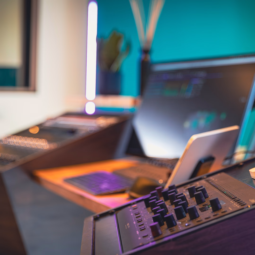 Nahaufnahme eines Audio-Mischpults in einem modernen Tonstudio mit unscharfen Monitoren im Hintergrund.