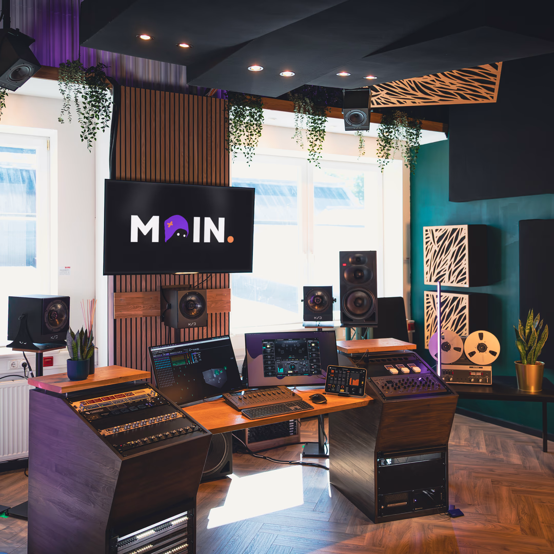 Modernes Tonstudio mit Mischpulten, Monitorlautsprechern, Computermonitoren und einem TV-Bildschirm mit der Aufschrift MOIN.