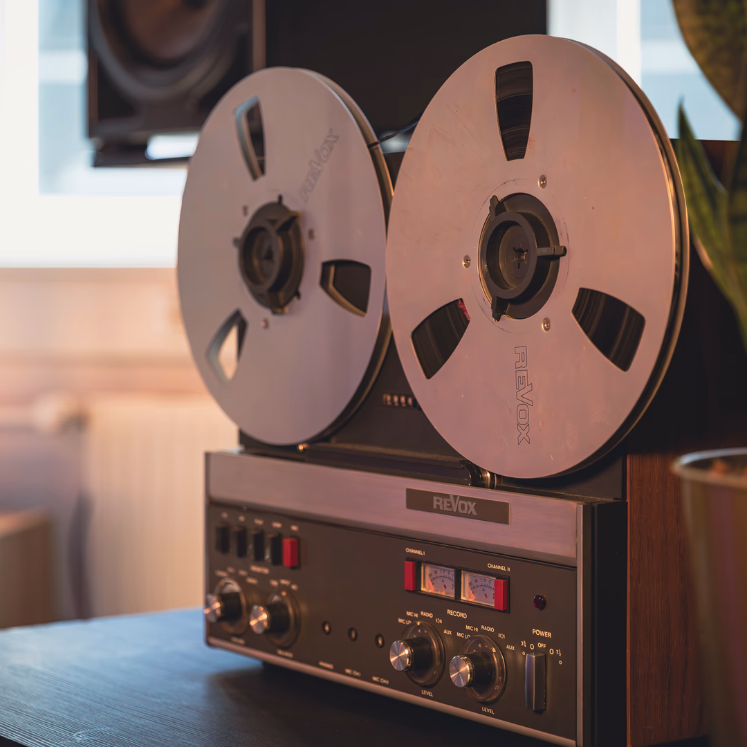 Nahaufnahme eines vintage Revox Tonbandgeräts mit zwei großen Spulen und Bedienknöpfen auf schwarzem Tisch.